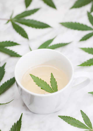 white mug with marijuana infusion with green leaf inside on marble table with leaves. topview.の写真素材