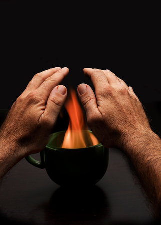 man's hands over cup with fire to warm up energy povertyの写真素材
