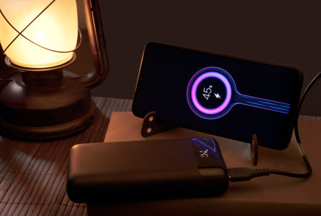 Smartphone with portable power bank energy battery, on book and oil lamp, energy poverty social...