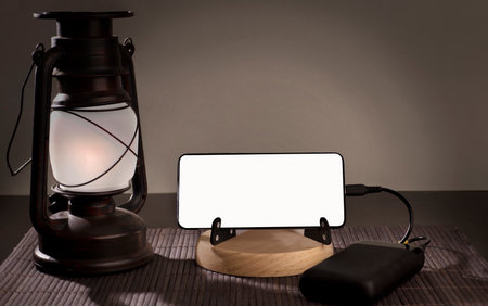 Smartphone with copy space, over wood and oil lamp, social problem energy poverty. background gray brown.の写真素材