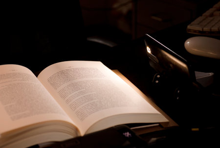 cell phone and power bank on the desk illuminates reading and study book with battery-powered computer in the background, energy poverty concept power outagesの写真素材