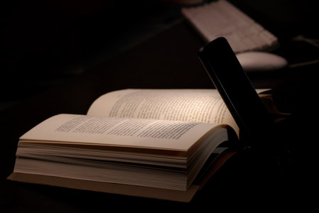 cell phone and power bank on the desk illuminates reading and study book with battery-powered computer in the background, energy poverty concept power outagesの写真素材