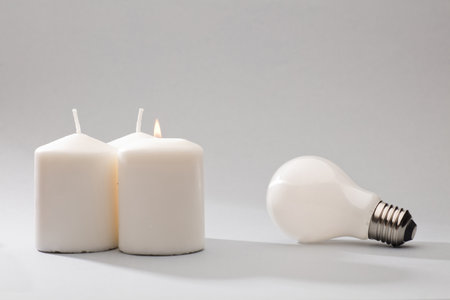 concept lack of electricity supply. three white candles and light bulb on gray backgroundの写真素材