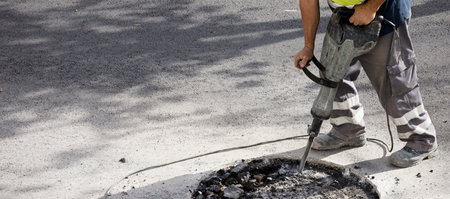 hydraulic hammer in the hands of an operator in uniform works the asphalt, space for text