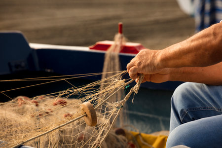 Fishing fishing net in the hands of fisherman. sew and repair the beach, sea in the backgroundの写真素材