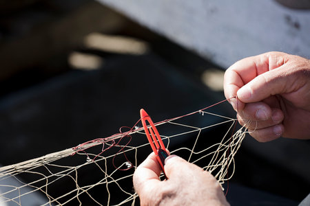 fishing net in the hands of fisherman, he weaves and repairs by sewing the nets with a needle and...