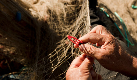 fishing net in the hands of fisherman, he weaves and repairs by sewing the nets with a needle and threadの写真素材