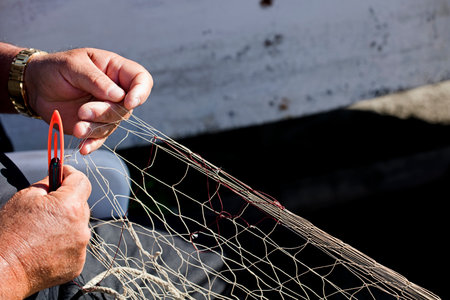 fishing net in the hands of fisherman, he weaves and repairs by sewing the nets with a needle and...