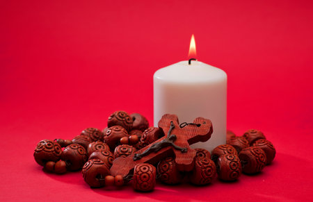 red wooden catholic rosary with lit white candle, on red background, space for textの写真素材