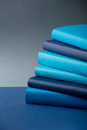 Stack of books Different tones of blue, on desk, with gray background