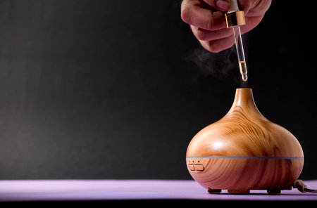wooden air freshener with steam of natural essences, man's hand with dispenser, purple and black backgroundの写真素材