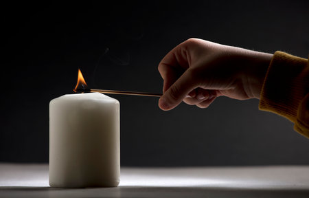 white candle with flame, little child hand with fire stick, black backgroundの写真素材