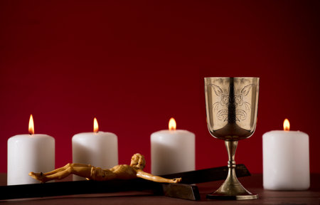 golden chalice with crucifix and burning candles red backgroundの写真素材
