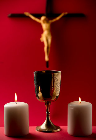 golden chalice with crucifix and burning candles red backgroundの写真素材