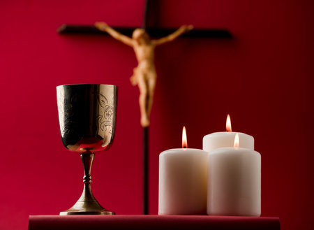 golden chalice with crucifix and burning candles red backgroundの写真素材