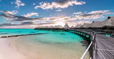 Scenic panoramic landscape view of luxury overwater bungalows at the beach and lagoon during sunset in Moorea, French Polynesia.の写真素材