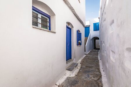 Narrow street between white traditional houses with blue door and window in town center of Amorgos, Greece.の写真素材