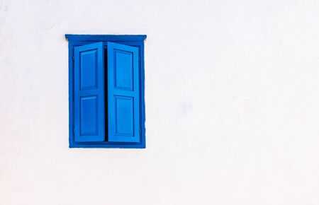 White wall with blue window and closed shutters. Greek style.