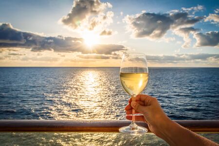 During sunset a female hand toasts the new year with a glass of white wine. Photo taken on a balcony of a cruise ship with a sea view.の写真素材