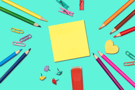 Bright back to school supplies with yellow sticky note on turquoise background. Flat lay.