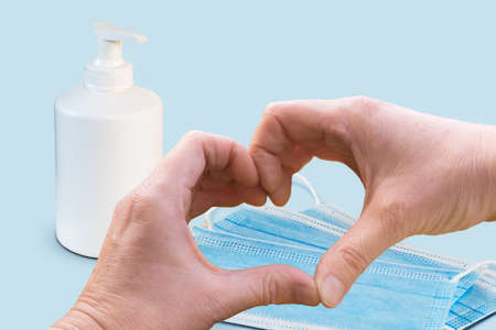 Preventing virus concept with heart shaped hands, protective face mask and soap bottle on blue background.の写真素材