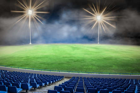 Football stadium field at night. Illuminated lights on the soccer field with blue empty seats.の写真素材