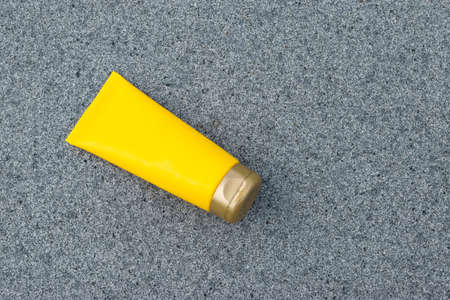 Yellow cream tube on a gray texture background. Flat lay. Mock-up.の写真素材