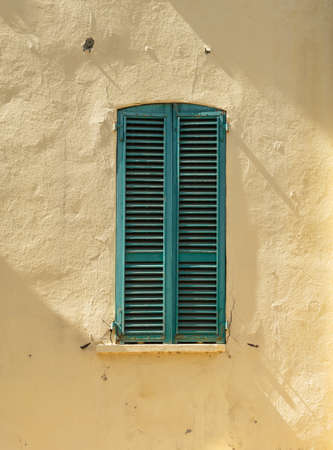 Old wooden window shutters closed against yellow wall.の写真素材