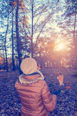 Young woman in warm clothes having fun with autumn leaves in the forest.の写真素材