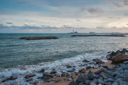 The armourstone wall and waves at the coast with the industrial estate behind.