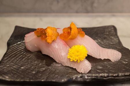 Kampachi sushi with Uni and Ikura on top on black ceramic plateの写真素材