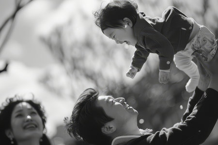A cheerful young child is lifted high by his father during a playful moment outside, with the mother watching lovingly.の素材