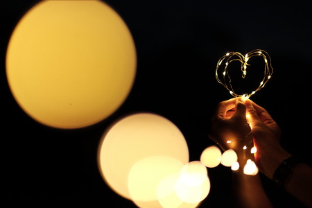 A lovely lighting heart shape in a man's hand with big bokeh lightingの写真素材