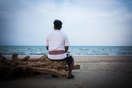 the young man sitting on the timber at the beachの写真素材