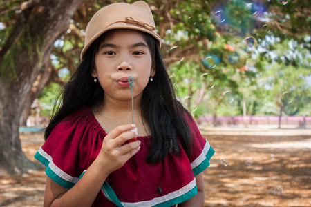 Little asian cute girl playing with bubble wand blowing soap bubbles in the garden backgroundの写真素材