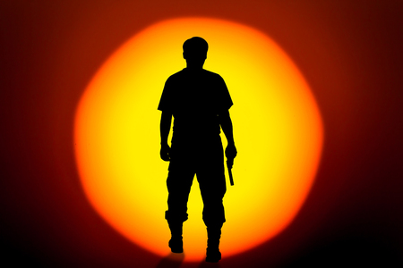 silhouette rear of man standing hand holding gun revolvers on big sunset background