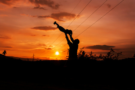 silhouettes of father and son play at mountain range and high voltage electricity pylon sunset backgroundの写真素材