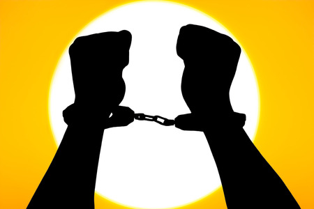 silhouette of hand in handcuffs on big sunset backgroundの写真素材