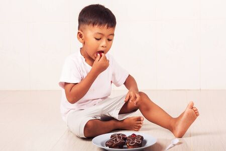 little boy eating chocolate cake in the roomの写真素材