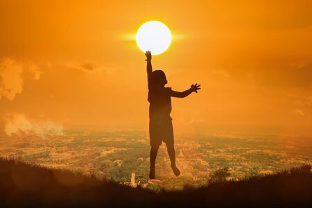 silhouette of boy happy jumping touch  the sun , sunset backgroundの写真素材