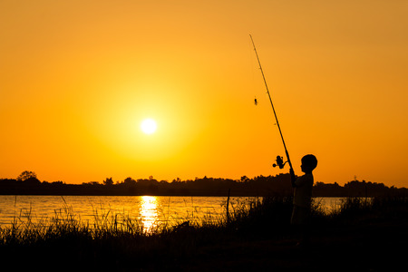 little boy fishing in the river sunset backgroundの写真素材