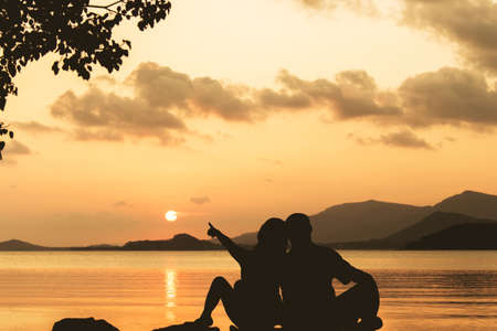 Silhouette of romance couple sitting on a rock in sunsetの写真素材