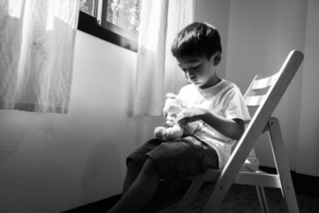 Blurry of little boy sitting alone on chair  at window in room,black and whiteの写真素材
