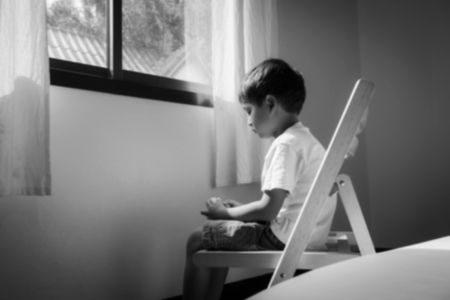 Blurry of little boy sitting alone on chair  at window in room,black and whiteの写真素材
