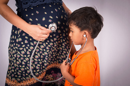 Cute little boy listen to a stethoscope belly of his pregnant momの写真素材
