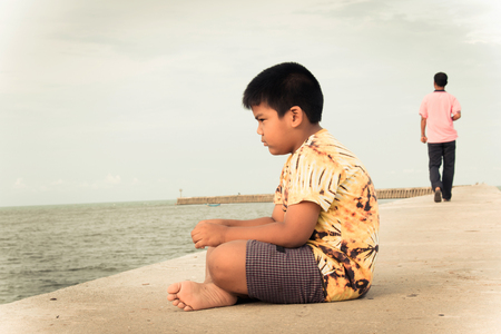 little boy unhappy sitting alone on bridge,vintage toneの写真素材