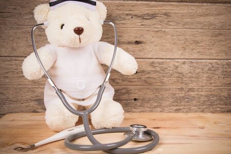 Cute white tebby bear wear nurse with stethoscope and thermometer on wooden background ,vintage toneの写真素材