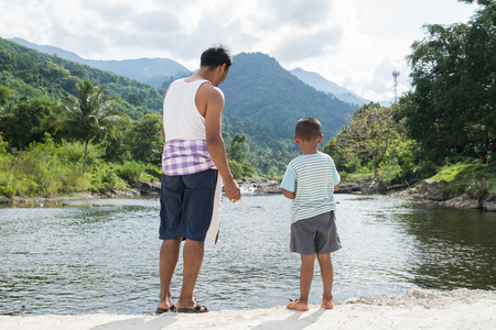 Dad and son feeding fish at riverの写真素材