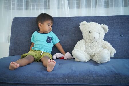 Cute little boy sitting on the sofa with teddy bearの写真素材
