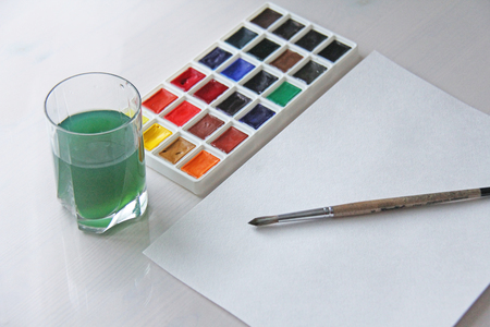 Watercolors, brushes, white sheet of paper and a glass of water for drawing. Hobbies and creativity.の写真素材